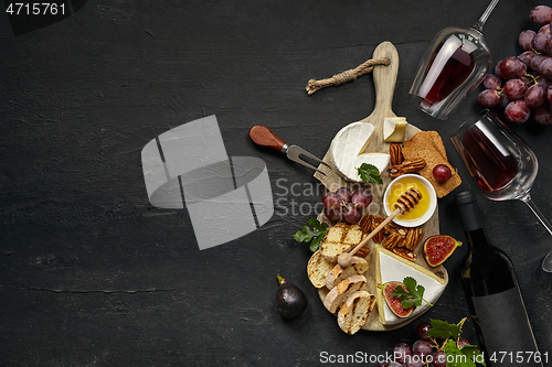 Image of Two glasses of red wine and cheese plate with fruit on the black stone