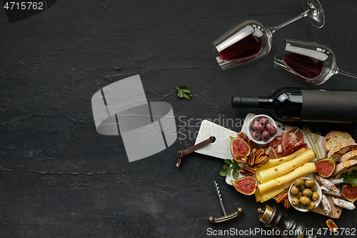 Image of Two glasses of red wine and cheese plate with fruit on the black stone