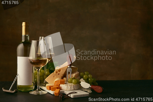 Image of Front view of tasty cheese plate with the wine bottle on dark studio background