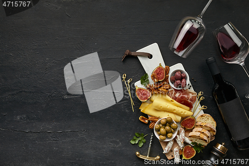 Image of Two glasses of red wine and cheese plate with fruit on the black stone