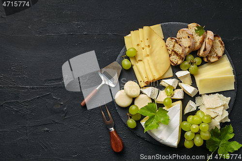 Image of Top view of tasty cheese plate with fruit on the black stone