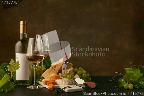 Image of Front view of tasty cheese plate with the wine bottle on dark studio background