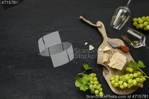 Image of Two glasses of white wine and a tasty cheese plate on a wooden kitchen plate.