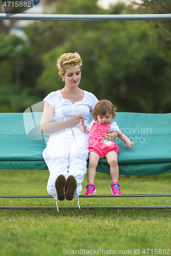 Image of mother and little daughter swinging at backyard