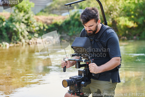 Image of a professionally equipped cameraman shoots in the water surrounded by beautiful nature.