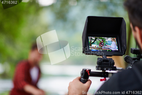 Image of a professionally equipped cameraman is filming a group of people having dinner by the river.