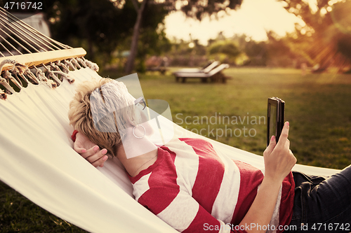 Image of woman using a tablet computer while relaxing on hammock