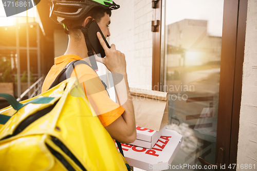 Image of Young man as a courier delivering pizza using gadgets