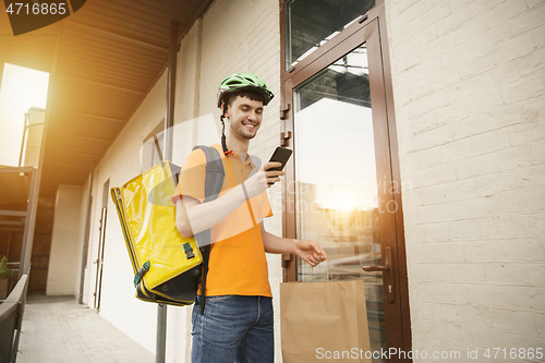 Image of Young man as a courier delivering pizza using gadgets