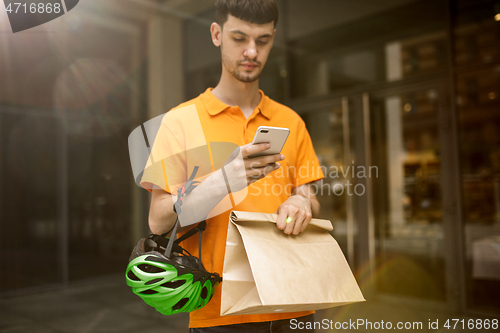 Image of Young man as a courier delivering package using gadgets