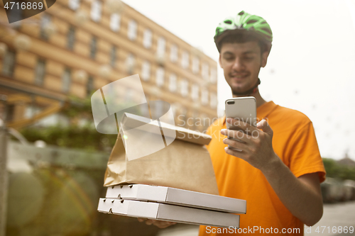 Image of Young man as a courier delivering pizza using gadgets