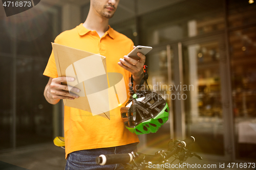 Image of Young man as a courier delivering package using gadgets