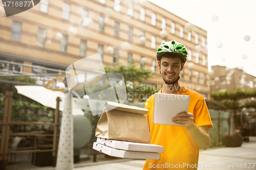 Image of Young man as a courier delivering pizza using gadgets