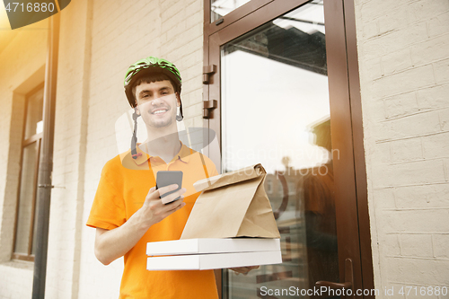 Image of Young man as a courier delivering pizza using gadgets