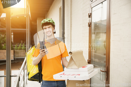 Image of Young man as a courier delivering pizza using gadgets