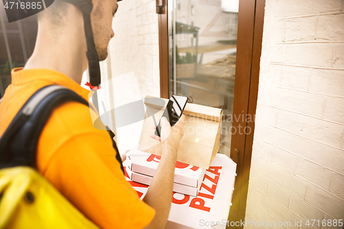 Image of Young man as a courier delivering pizza using gadgets