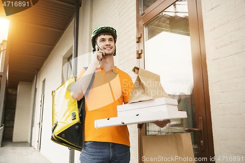 Image of Young man as a courier delivering pizza using gadgets