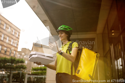 Image of Young woman as a courier delivering pizza using gadgets