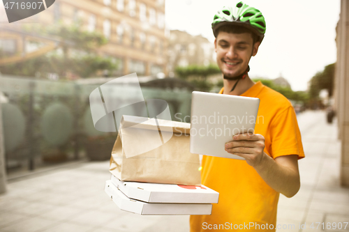 Image of Young man as a courier delivering pizza using gadgets