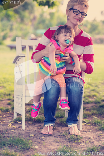 Image of mother and cute little daughter sitting on wooden bench