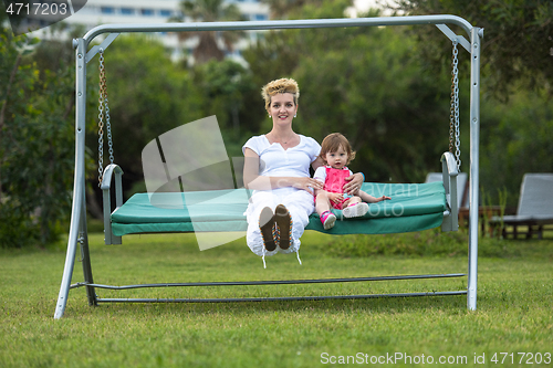 Image of mother and little daughter swinging at backyard