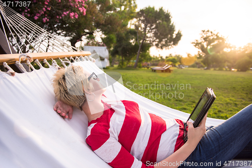 Image of woman using a tablet computer while relaxing on hammock