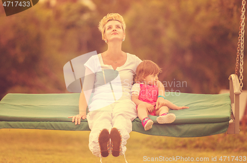 Image of mother and little daughter swinging at backyard