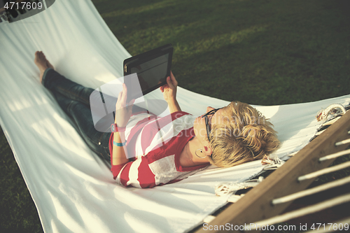 Image of woman using a tablet computer while relaxing on hammock