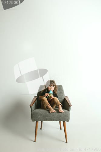 Image of Little child sitting and playing in armchair on white studio background