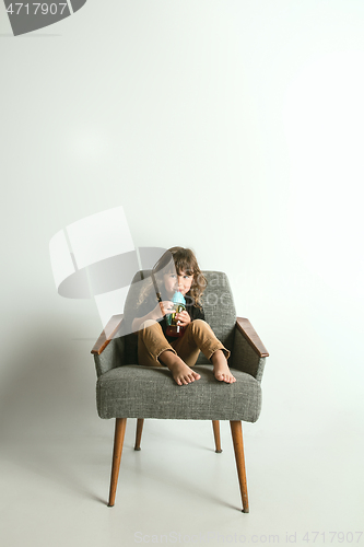 Image of Little child sitting and playing in armchair on white studio background