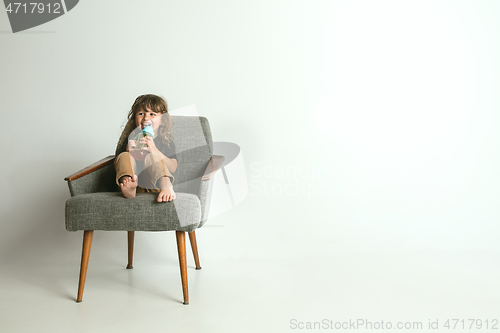 Image of Little child sitting and playing in armchair on white studio background
