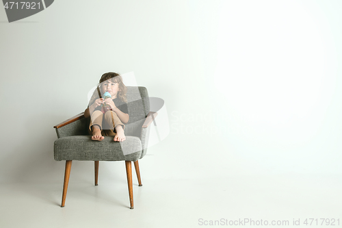 Image of Little child sitting and playing in armchair on white studio background