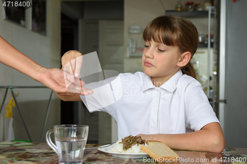 Image of To a sick girl before a meal, mother holds out medicine in her palm