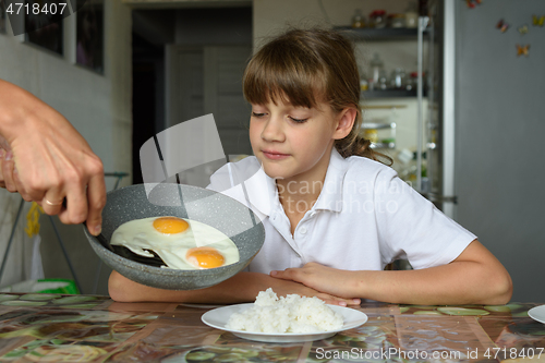 Image of Mom cooked scrambled eggs for lunch and puts them from the pan on the daughter\'s plate