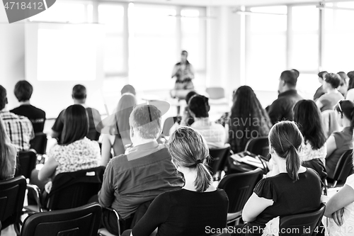 Image of Speaker giving a talk in conference hall at business meeting event. Rear view of unrecognizable people in audience at the conference hall.