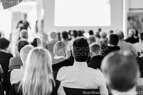 Image of Speaker giving a talk in conference hall at business meeting event. Rear view of unrecognizable people in audience at the conference hall.