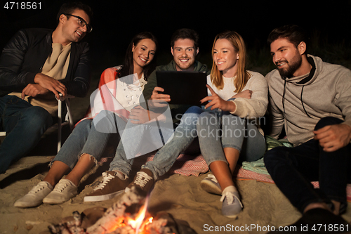 Image of friends with tablet pc at fire on beach at night