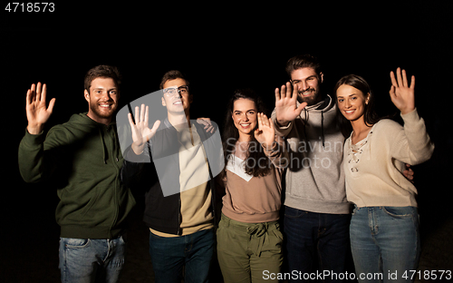 Image of happy smiling friends waving hands at night