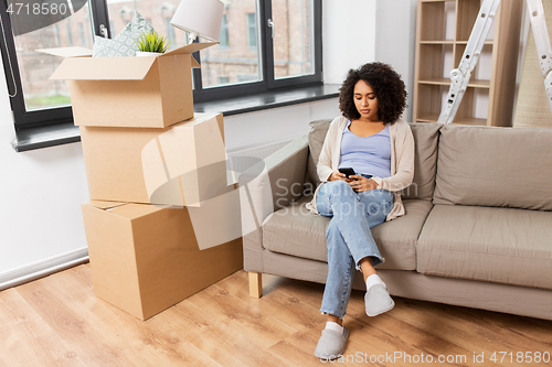 Image of woman with smartphone and boxes moving to new home