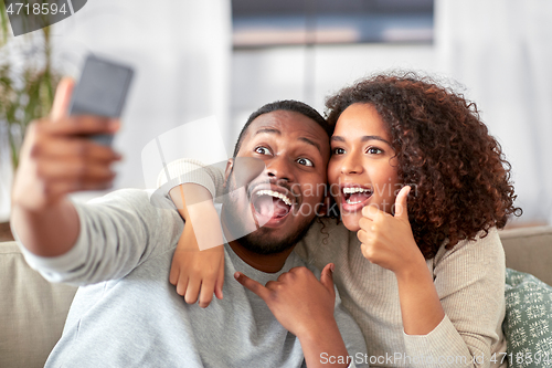 Image of happy couple with smartphone taking selfie at home