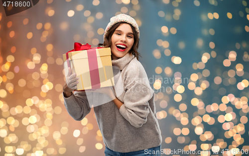 Image of young woman in knitted winter hat holding gift box