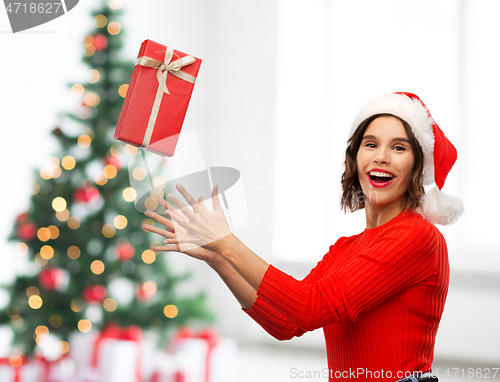 Image of happy young woman in santa hat catching gift box