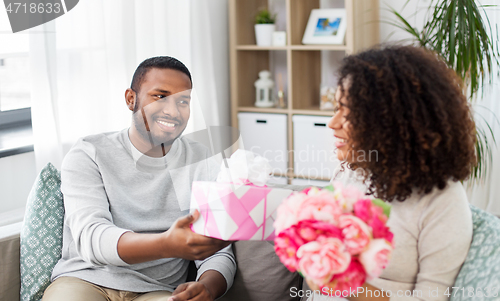 Image of happy couple with flowers and gift at home