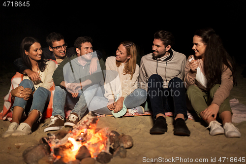 Image of group of friends sitting at camp fire on beach