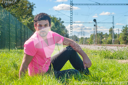 Image of Young man in orange sitting on the green grass
