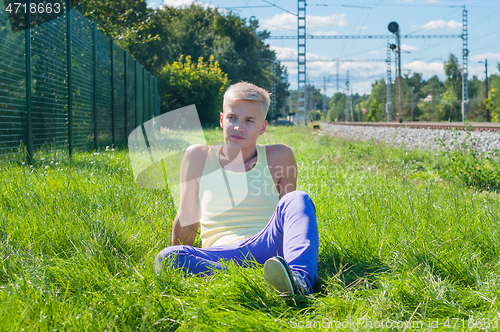 Image of Young man in orange sitting on the green grass