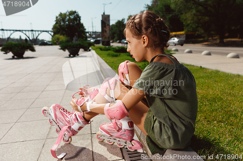 Image of Teenage girl in a helmet learns to ride on roller skates outdoors