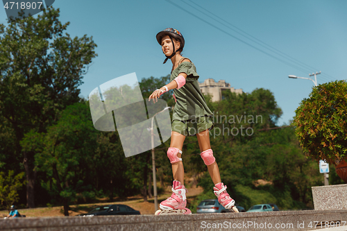 Image of Teenage girl in a helmet learns to ride on roller skates outdoors