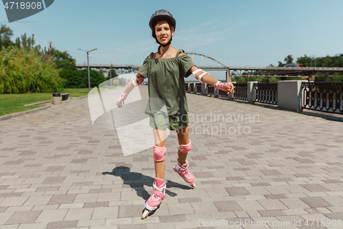 Image of Teenage girl in a helmet learns to ride on roller skates outdoors