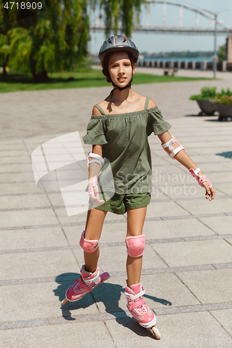 Image of Teenage girl in a helmet learns to ride on roller skates outdoors